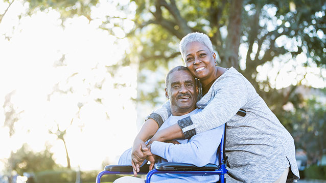 A woman hugs a man in a wheelchair in a park. Get answers to Supplemental Security Income FAQs in Oregon.