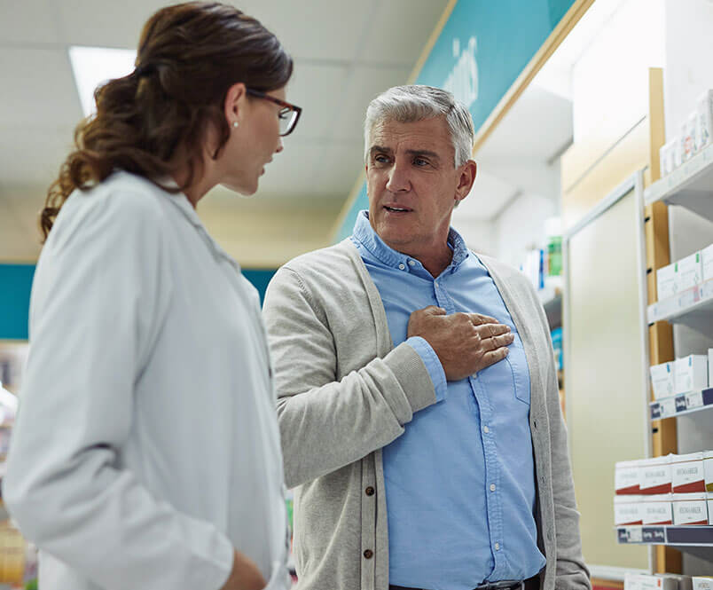 A man stands in a pharmacy talking to a woman in a white coat.