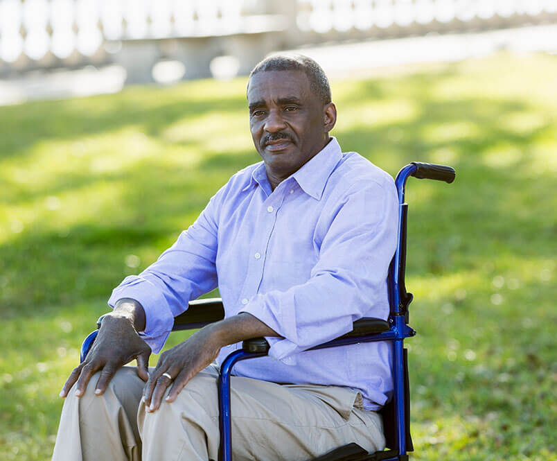 A man sits in a wheelchair in a park.