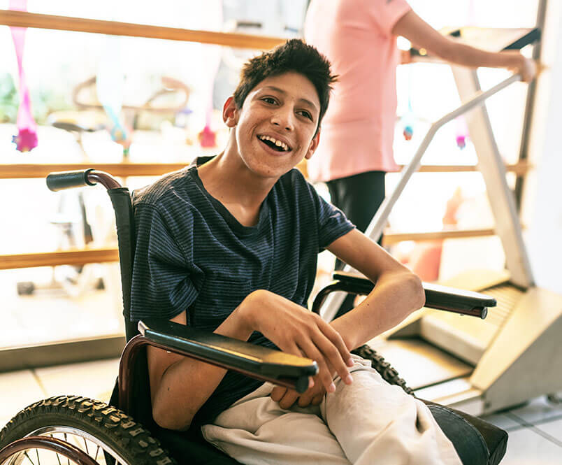 A boy sits in a wheelchair and smiles.